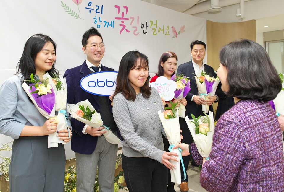 한국애브비 부서장들이 새로운 오피스에 봄이 왔음을 알리는 화사한 꽃들로 꾸며진 꽃길에서 첫 출근하는 직원들에게 꽃을 선물하고 있다. [사진=한국애브비 제공]